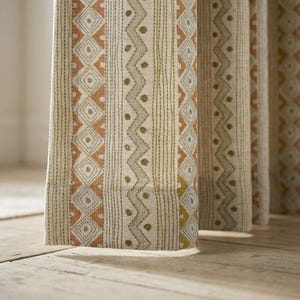 May include: Close-up of patterned fabric curtains. The curtains feature a repeating design of diamonds, zigzags, and vertical stripes in shades of beige, orange, and olive green. The fabric appears to be textured.
