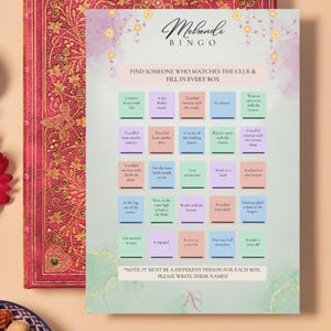 May include: A decorative Mehndi Bingo game card with a floral design. The card features a grid of boxes with prompts like "Traveled from another country" and "Is in the Bride's cousin". The card is on a table next to a decorative book.