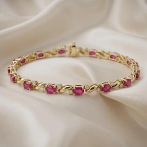 May include: A gold link bracelet featuring a repeating pattern of oval-cut red rubies and small round white diamonds. The metal links have a polished finish and the piece includes a secure box clasp closure with a safety latch mechanism.