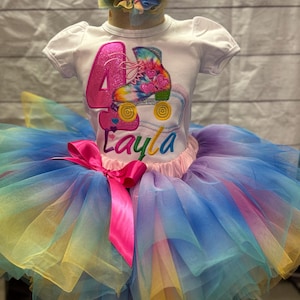 May include: A white t-shirt with a pink number 4 and a tie-dye roller skate design, paired with a multi-colored tutu skirt and a matching headband. The tutu features layers of blue, yellow, and purple tulle, and a pink satin bow. The name "Layla" is embroidered on the shirt.