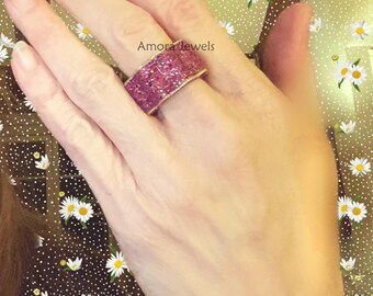 May include: A wide, pink gemstone ring with a gold band is displayed on a hand. The ring is encrusted with small, pink gemstones. The text "Amora jewels" is visible on the image.