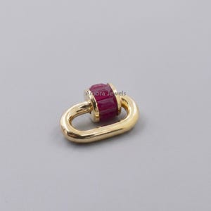 Könnte beinhalten: Ein goldfarbener Schmuckverschluss mit einem rechteckigen, tiefroten Edelstein in der Mitte. Der Verschluss ist oval geformt und hat ein Scharnierdesign. Der Markenname "Amora Jewels" ist im Hintergrund sichtbar.