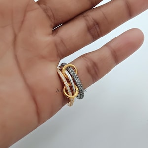 Könnte beinhalten: Ein Satz von drei ineinandergreifenden Ringen. Ein Ring ist goldfarben, ein anderer silberfarben und der dritte schwarz mit kleinen, funkelnden Steinen. Die Ringe sind durch goldfarbene Reifen verbunden.