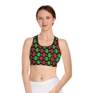 May include: Black sports bra with a repeating pattern of red and green gummy bears and cherries. The bra has a scoop neck and racerback design. The model is wearing white bottoms.