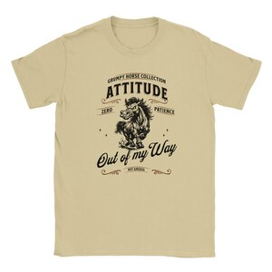 Könnte beinhalten: Beiges T-Shirt mit einer schwarz-weißen Illustration eines Pferdes und dem Text "Grumpy Horse Collection Attitude Zero Patience Out of my Way Not Amused". Das T-Shirt hat einen Rundhalsausschnitt und kurze Ärmel.
