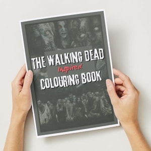 May include: A person holds a colouring book titled "The Walking Dead Inspired Colouring Book". The cover displays grayscale images of zombies and the show's title in white and red text.