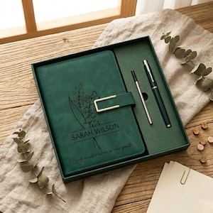 Peut inclure: Un ensemble de journal et de stylos verts dans une boîte cadeau. Le journal présente un motif floral, le nom "SARAH WILSON" et la citation "Each chapter where in new growth". L'ensemble comprend un stylo et un stylo à bille.