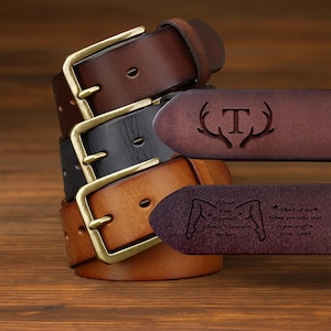 May include: A selection of leather belts in shades of brown, black, and tan. Each belt features a brass buckle. One belt is engraved with the letter "T" and antlers, and another has a personalized message.