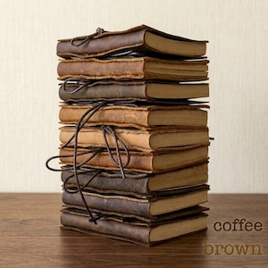 May include: A pile of leather-bound journals in shades of brown, tied together with a dark brown cord. The journals are stacked on a wooden surface. The text "coffee brown" is visible in the image.