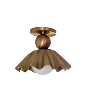 May include: A brass-toned ceiling light fixture with a round base and a spherical accent. The fixture features a ruffled, flared shade and a white, spherical light diffuser. The overall design is elegant and decorative, suitable for interior lighting.