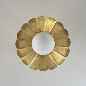 May include: A gold-colored, scalloped-edge ceiling light fixture with a white, spherical light bulb in the center. The fixture has a flower-like design and is mounted on a white ceiling.
