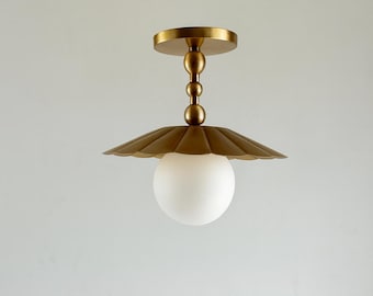 May include: A brass ceiling light fixture with a scalloped shade and a frosted globe. The fixture has a round base and a series of decorative spheres connecting the base to the shade. The overall design is elegant and modern.