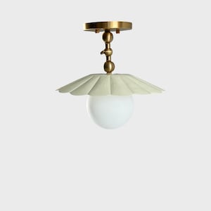May include: A ceiling light fixture with a brass finish and a cream-colored, scalloped shade. The light has a white, spherical bulb. The fixture is designed to be mounted on the ceiling.