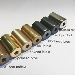 May include: A collection of cylindrical metal objects in various finishes, including antique patina, polished brass, brushed brass, raw brass, blackened brass, antique black, and polished chrome. Each cylinder has a hole in the center. The text labels each finish.