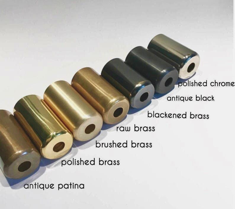 May include: A collection of cylindrical metal objects in various finishes, including antique patina, polished brass, brushed brass, raw brass, blackened brass, antique black, and polished chrome. Each cylinder has a hole in the center. The text labels each finish.