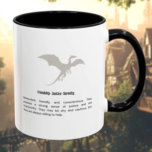 Puede incluir: Taza de cerámica blanca con asa e interior negros. La taza presenta una ilustración de dragón gris y el texto "Amistad Justicia Serenidad". Texto adicional describe las características del dragón. La taza está sobre un fondo borroso.