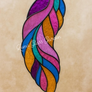 Pode incluir: Uma peça de vitral em forma de pena estilizada, com cores vibrantes, incluindo roxo, rosa, azul, turquesa e laranja. O vidro é contornado em preto. O texto "Luna Glass Garden" está escrito no vidro.