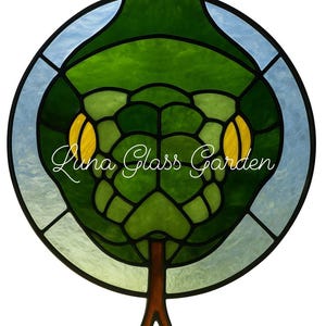 May include: Circular stained glass art piece depicting a green snake head with yellow eyes and a brown tree trunk base. The text "Luna Glass Garden" is written in cursive. The background is light blue.