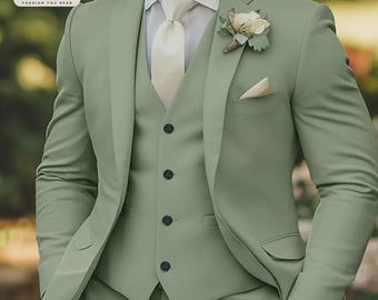 May include: A three-piece suit in a soft green color. The suit includes a blazer, vest, and trousers. The blazer has a notched lapel and a pocket square. A white dress shirt and cream-colored tie are worn underneath. A floral boutonniere is pinned to the lapel.
