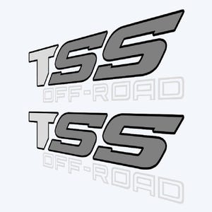 May include: Two gray and white TSS Off-Road decals. The decals are angled, with the letters TSS in a stylized font. The words "OFF-ROAD" are printed below the letters in a lighter gray color. The image has a white background.