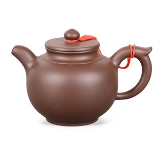 Op de afbeelding: Bruine keramische theepot met een deksel en een gebogen handvat. De theepot heeft een tuit en een kleine knop op het deksel. Een rood koord is bevestigd aan het deksel en het handvat. De theepot is ontworpen voor het zetten van thee.