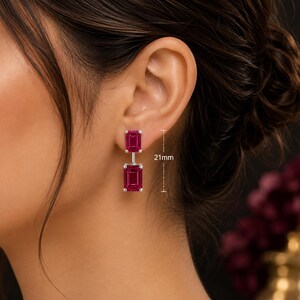 Pode incluir: Um par de brincos pendentes com duas pedras retangulares de corte esmeralda em vermelho rosado profundo, engastadas em metal prateado. Os brincos t&ecirc;m um comprimento vertical total de 21mm, conforme indicado pelas linhas de medi&ccedil;&atilde;o vis&iacute;veis.