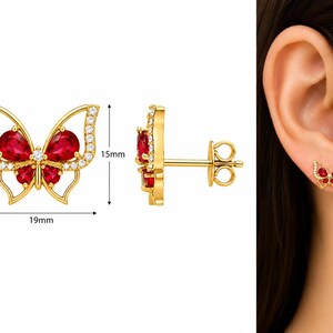 May include: Gold butterfly stud earrings featuring pear-shaped red stones and small clear accent stones. The butterfly design measures 19mm in width and 15mm in height. The earrings include a post and butterfly back closure for secure wear.