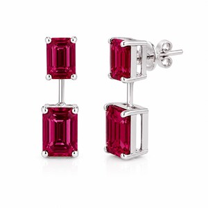 Pode incluir: Um par de brincos pendentes com duas pedras retangulares de corte esmeralda em vermelho profundo, engastadas em metal prateado polido. Cada brinco consiste numa pedra mais pequena suspensa sobre uma maior, com fecho de press&atilde;o.