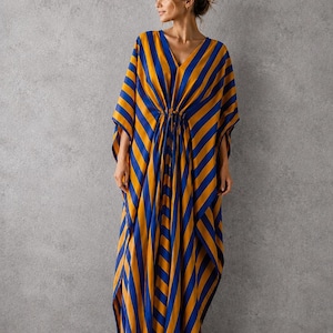 May include: A floor-length kaftan dress featuring a bold diagonal stripe pattern in vibrant royal blue and golden yellow. The garment has a deep V-neckline, wide flowing sleeves, and a central drawstring waist detail that creates soft vertical folds.