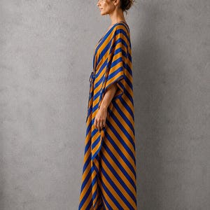 May include: A floor-length kaftan featuring a bold diagonal stripe pattern in vibrant mustard yellow and deep royal blue. The garment has wide, flowing sleeves, a V-neckline, and a relaxed silhouette that drapes loosely down to the ankles.