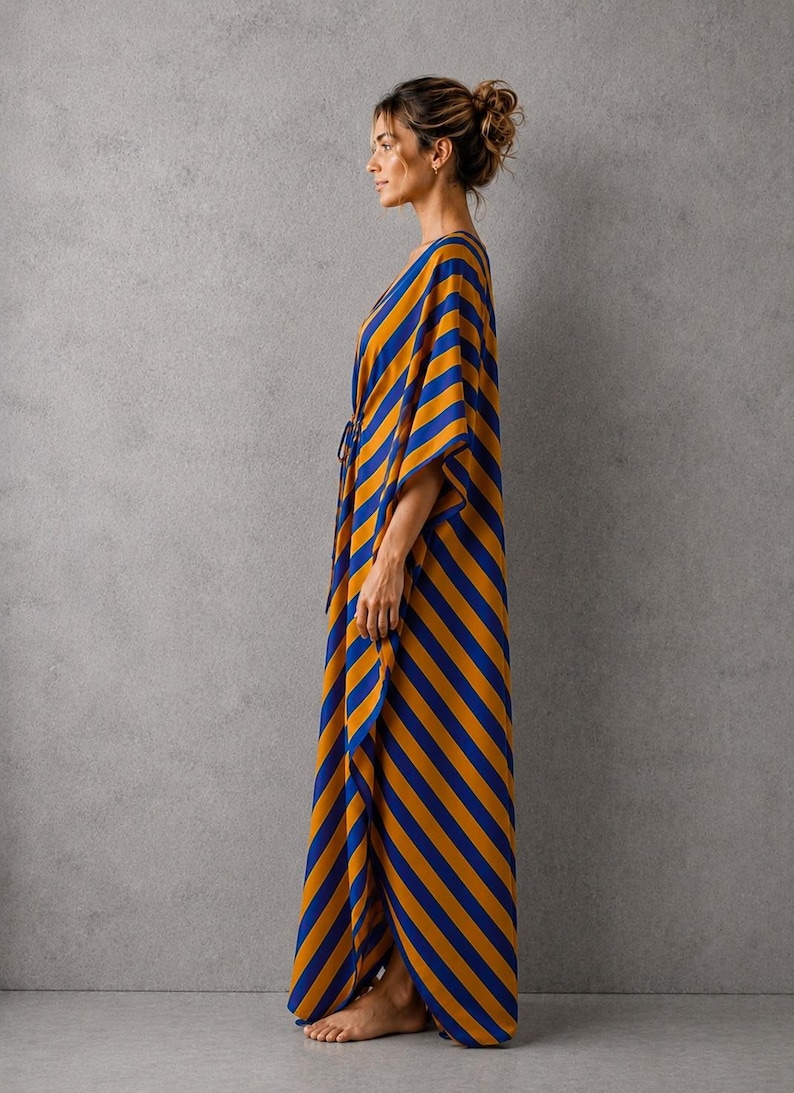 May include: A floor-length kaftan featuring a bold diagonal stripe pattern in vibrant mustard yellow and deep royal blue. The garment has wide, flowing sleeves, a V-neckline, and a relaxed silhouette that drapes loosely down to the ankles.