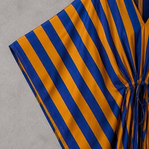 May include: A kaftan featuring a bold vertical stripe pattern in vibrant royal blue and golden yellow. The garment has a V-neckline, wide sleeves, and a drawstring waist detail with matching fabric ties that create a gathered effect at the center.