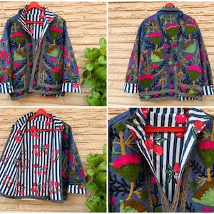 Può includere: Una giacca reversibile caratterizzata da un esterno blu con vivaci ricami floreali in rosa e verde, e una fodera interna a contrasto con un motivo a righe verticali bianche e blu navy accentuato da piccole illustrazioni di frutti rossi.