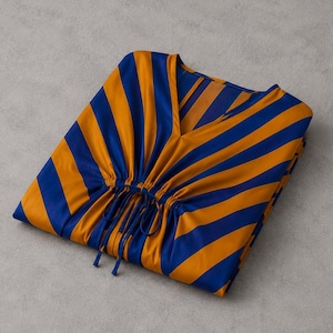 May include: A V-neck tunic featuring a bold pattern of alternating royal blue and golden orange diagonal stripes. The garment includes a gathered waist detail with thin, matching blue fabric drawstrings that hang down from the center front.