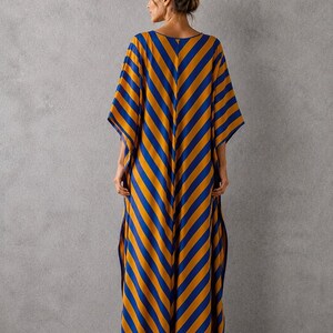 May include: A floor-length kaftan dress featuring a bold diagonal stripe pattern in vibrant mustard yellow and royal blue. The garment has a loose, flowing silhouette with wide, short sleeves and side slits that extend from the hem to the mid-thigh.