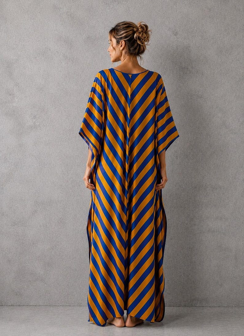 May include: A floor-length kaftan dress featuring a bold diagonal stripe pattern in vibrant mustard yellow and royal blue. The garment has a loose, flowing silhouette with wide, short sleeves and side slits that extend from the hem to the mid-thigh.