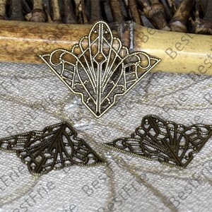 May include: Three antique gold metal corner embellishments with intricate filigree designs. The embellishments are in the shape of a triangle with a pointed top and a curved bottom.