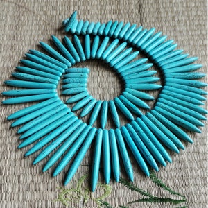 Peut inclure: Un collier bleu turquoise composé de longues perles fines et pointues. Les perles sont disposées en cercle, créant un effet de soleil.