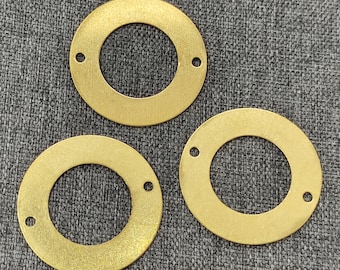 May include: Three gold-colored metal rings with a circular hole in the center. The rings are on a gray textured surface.