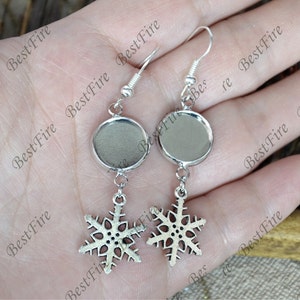 May include: Silver snowflake earrings with a round, silver, blank, bezel setting. The earrings are perfect for adding a personal touch with a photo or other embellishment.