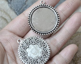 May include: Two silver-toned metal pendant charms. One charm is round with a smooth surface and a beaded edge. The other charm is round with a decorative, swirling pattern.