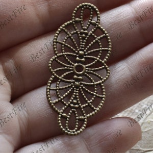 May include: A bronze filigree pendant with a circular design. The pendant has a delicate, intricate pattern and is perfect for adding a touch of elegance to jewelry projects.