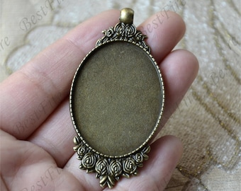 Puede incluir: Un colgante de color bronce con un inserto redondo de vidrio transparente y un diseño floral decorativo alrededor del borde.