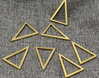 May include: A set of eight gold-toned triangle-shaped metal charms. The charms are all the same size and shape, and they are arranged in a random pattern on a gray fabric background.