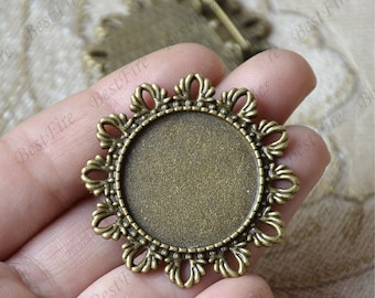 May include: A bronze-colored metal frame with a decorative, ornate design. The frame is round and has a smooth, flat surface in the center. It is designed to hold a round, flat object, such as a cameo or a photograph.