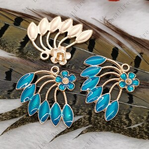 May include: Gold-toned metal floral embellishments with teal enamel leaves and flower accents. The jewelry findings feature intricate details and are suitable for crafting earrings, pendants, or other decorative projects. The design includes a flower and leaf motif.