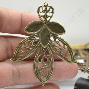 May include: A gold-toned metal pendant with a filigree design in the shape of a stylised flower. The pendant has a hole at the top for attaching a chain or cord.