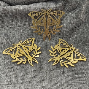 Puede incluir: Tres adornos de mariposa de metal dorado con diseños intrincados. Cada mariposa tiene un diseño de rama frondosa alrededor.