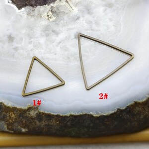 Pode incluir: Dois quadros triangulares de metal na cor bronze de tamanhos diferentes. O quadro menor está rotulado como 1# e o maior como 2#. Os quadros são abertos no centro e possuem um perfil fino e plano, apresentados como componentes de joalheria.