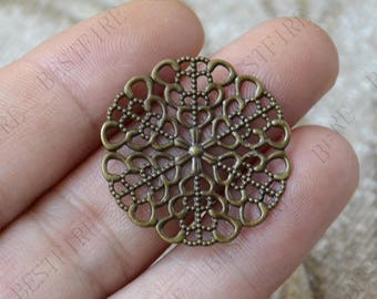 May include: A bronze filigree charm with a circular design. The charm has a delicate, intricate pattern of small circles and loops.